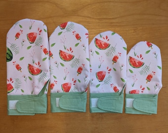Könnte beinhalten: Vier Ofenhandschuhe mit weißem Hintergrund, verziert mit Wassermelonenstücken, Eis am Stiel und grünen Blättern. Die Handschuhe haben eine grüne Manschette mit Klettverschluss.