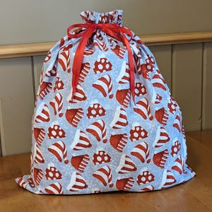 May include: A blue and red Christmas gift bag with a snowflake and Santa hat pattern. The bag is tied with a red ribbon.
