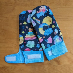 Puede incluir: Dos calientamanos de tela azul y negro con un estampado colorido de animales y estrellas. El texto "Sweet Dreams" está impreso en uno de los calientamanos.