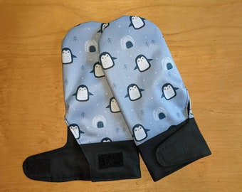 Könnte beinhalten: Ein Paar blaue Ofenhandschuhe mit einem Pinguin-Muster. Die Handschuhe haben schwarze Bänder und Klettverschlüsse.