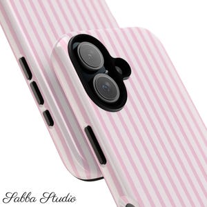 Op de afbeelding: Twee roze en wit gestreepte telefoonhoesjes. De hoesjes hebben een glanzende afwerking en een zwart cameramodule. De tekst "Sabba Studio" staat onderaan de afbeelding.
