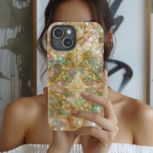 以下が含まれることがあります： 花柄デザインの装飾的な携帯電話ケース。ケースは、ピンク、緑、金の色合いの重なり合う形状のパターンと、金色のアクセントを備えた真珠光沢仕上げが特徴です。携帯電話ケースにはデュアルレンズカメラが付いています。