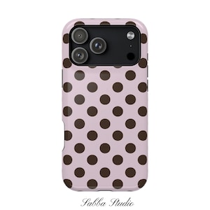 Könnte beinhalten: Eine rosa Handyhülle mit einem Muster aus dunkelbraunen Polka-Dots. Die Hülle hat einen Kameraausschnitt für eine Dreifach-Objektiv-Kamera. Der Text "Sabba Studio" ist unten auf der Hülle in einer Schriftart geschrieben.