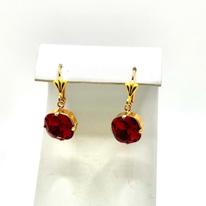 May include: A pair of gold dangle earrings with red gemstone drops. The earrings have a simple design and are perfect for everyday wear.