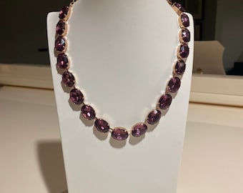 May include: A purple crystal necklace with oval-shaped stones and a rose gold chain.