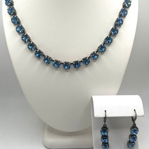 以下が含まれることがあります： ネックレスとイヤリングのセット。ネックレスはシンプルなチェーンに青いクリスタルが並んでいます。イヤリングは、それぞれ3つの青いクリスタルがついたドロップ型のイヤリングです。