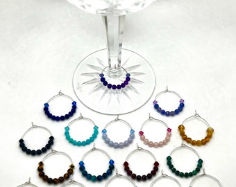 May include: Set of 18 colorful glass bead wine glass charms. Each charm features a different color and style of beads, including clear, blue, green, purple, pink, brown, and gray.