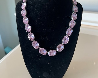 May include: A silver chain necklace with large, oval-shaped, light purple rhinestones.