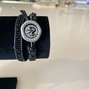 Black micro faceted spinel beads in dark grey metallic leather double wrap bracelet with silver tone fluer de lis button.