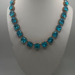 May include: A turquoise blue crystal necklace with gold-toned metal accents. The necklace is made of round, faceted crystals that are strung together on a thin chain.
