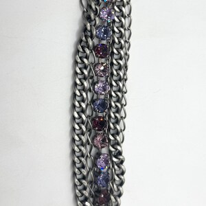 May include: A silver-toned bracelet featuring multiple chain strands. A central row of colorful, round gemstones in shades of purple and pink adds a pop of color. The bracelet has a toggle clasp for closure.