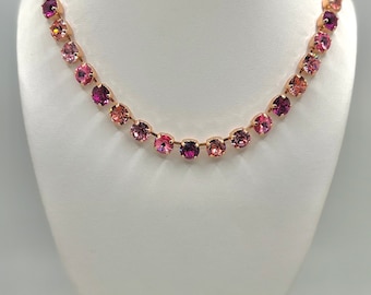 May include: A rose gold necklace with a graduated array of pink and purple crystals. The necklace is displayed on a white bust form, showcasing the varying shades of the gemstones.