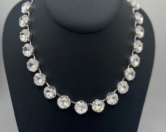Puede incluir: Un collar de plata con grandes diamantes de imitación redondos y transparentes.