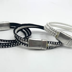 May include: Three wrap bracelets with magnetic clasps. One is black with silver-colored studs, another is black with clear studs, and the third is white with clear studs. The bracelets are displayed on a white surface.