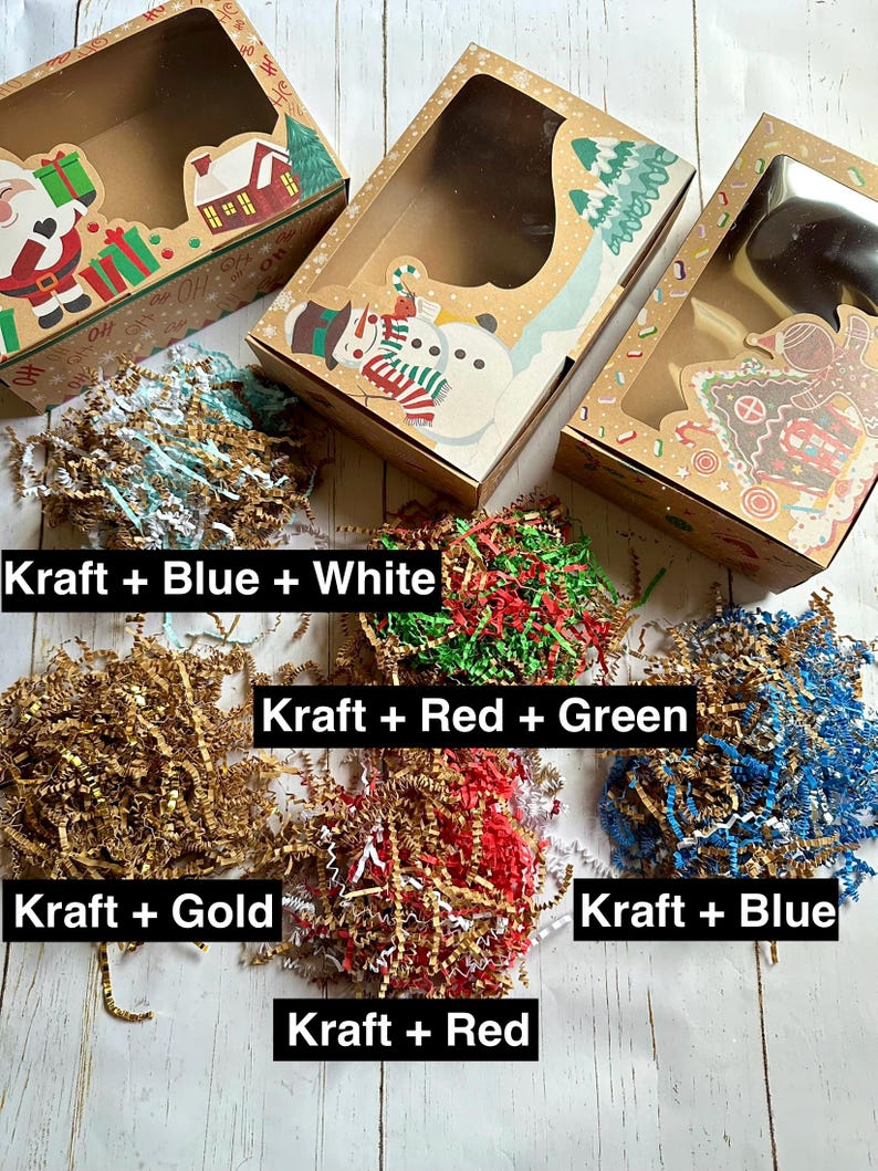 May include: Kraft paper gift boxes with clear windows, decorated with holiday-themed illustrations. The boxes are paired with shredded paper in various colors, including blue, white, gold, red, and green, with text labels.