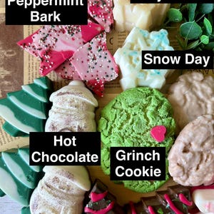 May include: A collection of festive, decorative soaps in various shapes and colors. The soaps include peppermint bark, Christmas trees, snow day, hot chocolate, Grinch cookie, and cozy winter designs. The image includes the text "Peppermint Bark", "Cozy Winter", "Snow Day", "Hot Chocolate", and "Grinch Cookie".