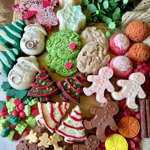 May include: A collection of festive, colorful soaps and candies in various shapes. Includes green and white striped tree soaps, snowman soaps, gingerbread men, and star-shaped soaps. Also features pink and white candies and chocolate bark.