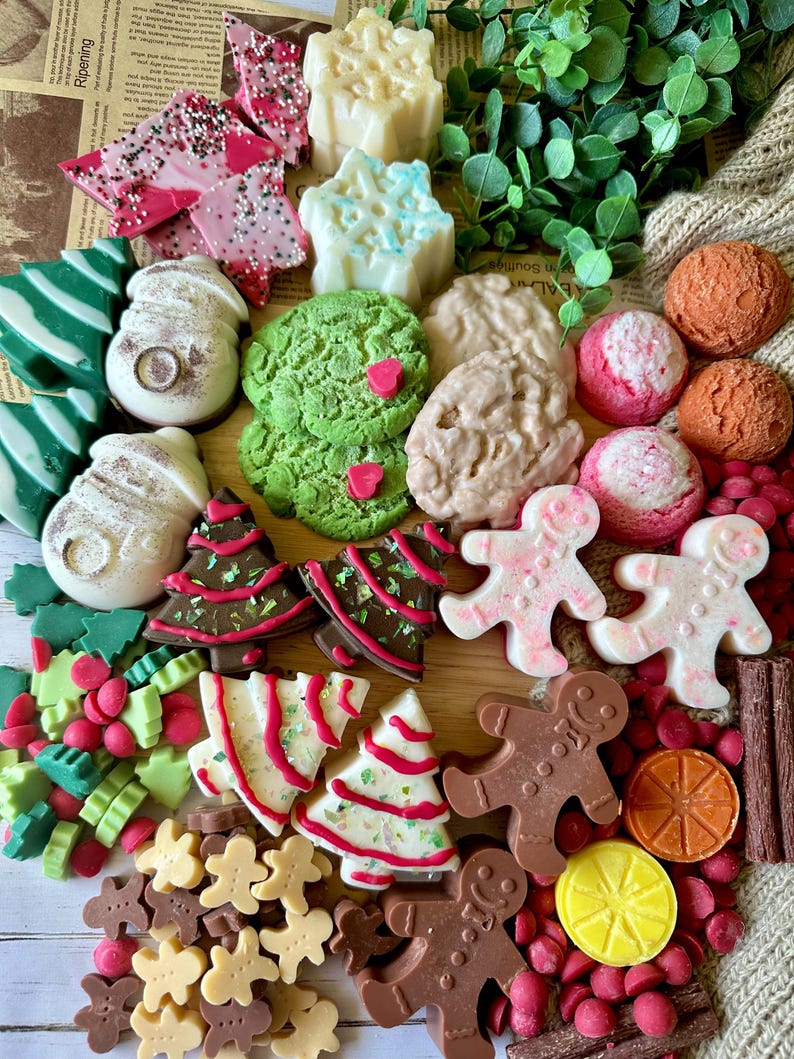 May include: A collection of festive, colorful soaps and candies in various shapes. Includes green and white striped tree soaps, snowman soaps, gingerbread men, and star-shaped soaps. Also features pink and white candies and chocolate bark.