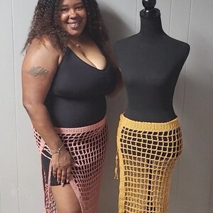 Puede incluir: Una mujer y un maniqu&iacute; exhiben faldas de ganchillo. La falda de la mujer es rosa claro, la del maniqu&iacute; es amarillo mostaza. Ambas faldas presentan un dise&ntilde;o de red y una abertura lateral alta, mostrando moda artesanal.
