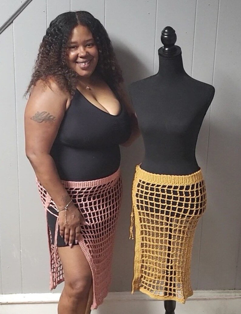 Puede incluir: Una mujer y un maniqu&iacute; exhiben faldas de ganchillo. La falda de la mujer es rosa claro, la del maniqu&iacute; es amarillo mostaza. Ambas faldas presentan un dise&ntilde;o de red y una abertura lateral alta, mostrando moda artesanal.