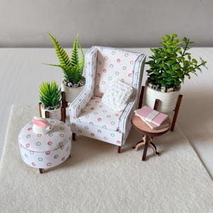 May include: A miniature dollhouse furniture set featuring a wingback chair and round ottoman with a white fabric patterned with small red and green circles, a small wooden side table with two books, two potted green plants, and a white rabbit figurine.