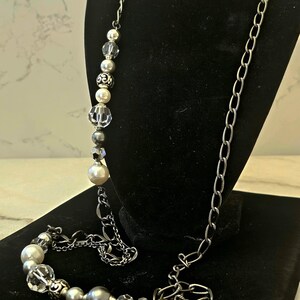 Puede incluir: Un collar largo de cadena plateada con una cadena plateada y cuentas de perlas blancas y cristal. El collar se muestra sobre un fondo de terciopelo negro. Cee Jayes Treasures 23 de octubre de 2024 12:51 PM