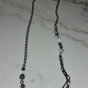 Puede incluir: Un collar de cadena negra con cuentas plateadas y blancas. El collar tiene un dise&ntilde;o de cadena doble y presenta una variedad de formas y tama&ntilde;os de cuentas.