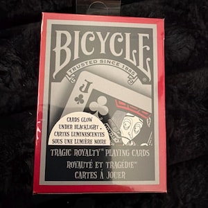 May include: A Bicycle playing card deck with a red border and a black and gray design. The box features the text "Bicycle Trusted Since 1885" and "Tragic Royalty Playing Cards". The cards glow under blacklight.