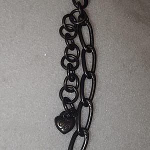 Puede incluir: Un collar de cadena de metal negro con un cierre en forma de coraz&oacute;n. El cierre tiene un peque&ntilde;o dije en forma de coraz&oacute;n con la letra "B" en &eacute;l.