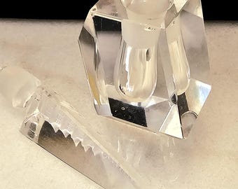 Puede incluir: Un tapón de botella de vidrio transparente con un diseño facetado y geométrico. El tapón tiene una punta puntiaguda y una parte superior redonda y hueca.