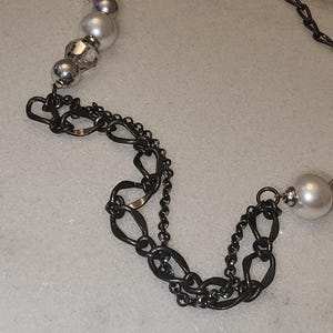 Puede incluir: Un collar de cadena plateado y negro con cuentas blancas y transparentes. La cadena est&aacute; hecha de dos estilos diferentes de eslabones, uno es un eslab&oacute;n ovalado simple y el otro es un dise&ntilde;o m&aacute;s intrincado.