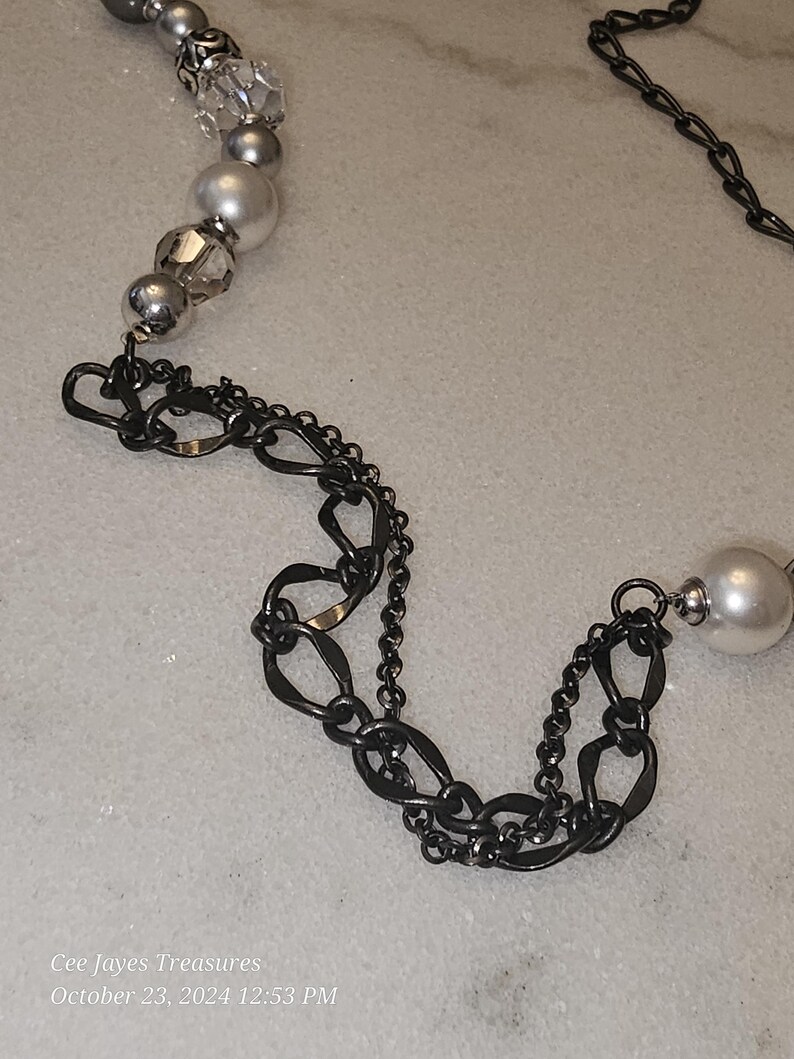 Puede incluir: Un collar de cadena plateado y negro con cuentas blancas y transparentes. La cadena est&aacute; hecha de dos estilos diferentes de eslabones, uno es un eslab&oacute;n ovalado simple y el otro es un dise&ntilde;o m&aacute;s intrincado.