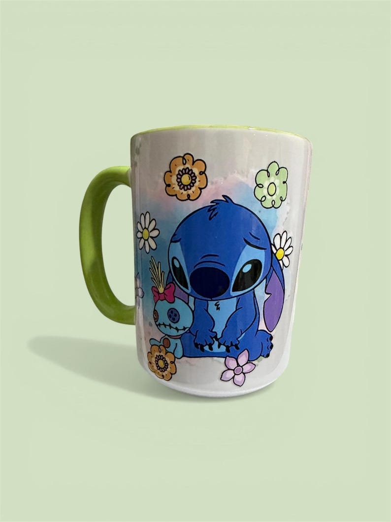 Pu&ograve; includere: Tazza in ceramica bianca con manico e bordo verdi, raffigurante un personaggio blu dei cartoni animati e un altro pi&ugrave; piccolo. La tazza &egrave; decorata con fiori colorati e uno sfondo ad acquerello. Un design divertente e stravagante.