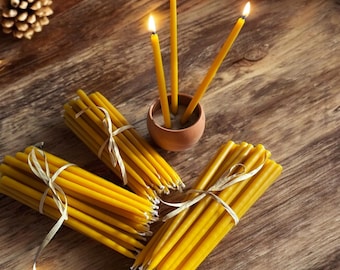 May include: A bundle of yellow beeswax candles tied with twine, with three lit candles in a small terracotta pot on a wooden surface.