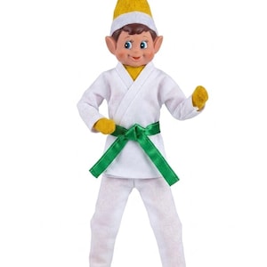 May include: A doll dressed in a white martial arts uniform with a green satin belt. The doll has brown hair, pointed ears, and wears a yellow pointed hat, yellow gloves, and yellow shoes. The figure stands in a pose with arms slightly bent.