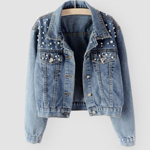 K&ouml;nnte beinhalten: Eine hellblaue Jeansjacke mit Perlenbesatz an den Schultern und den vorderen Taschen.