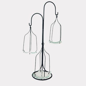 May include: A black metal decorative stand with three hanging glass holders. The stand has a curved design with a circular base and a hook at the top of each holder. The glass holders have a scalloped edge.