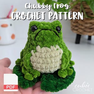 Op de afbeelding: Een groen gehaakt kikkerknuffeltje met een lichtcr&egrave;mekleurige buik, zwarte plastic ogen en een textuur van garen, zittend op een groen gehaakt waterlelieblad. De afbeelding bevat de tekst Chubby Frog CROCHET PATTERN en een PDF-pictogram.