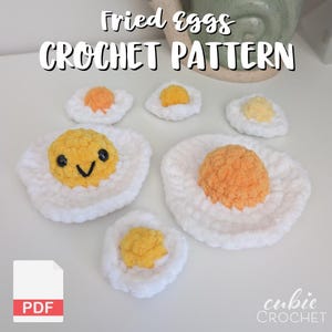 Puede incluir: Una colección de huevos fritos de ganchillo hechos a mano en varios tamaños. Los huevos presentan 'claras' blancas y 'yemas' amarillas o naranjas. Un huevo tiene una cara sonriente. El texto "Fried eggs CROCHET PATTERN" está en la parte superior.