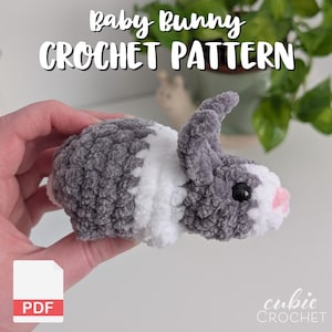 May include: A crocheted baby bunny in gray, white, and pink. The bunny has a fluffy texture and black eyes. The image includes the text "Baby Bunny Crochet Pattern" and a PDF icon.