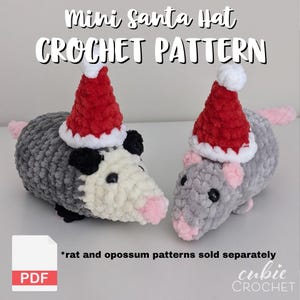 May include: Two crocheted opossum and rat figures wearing mini Santa hats. The opossum is gray and white, and the rat is gray. The hats are red with white trim. The image includes the text "Mini Santa Hat CROCHET PATTERN" and "PDF".