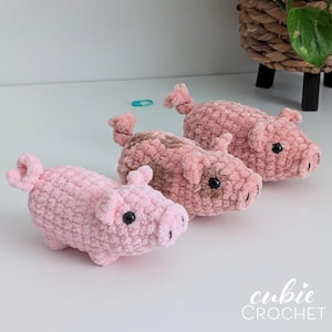 May include: Three handmade crochet plush pigs made from soft, textured pink yarn. Each pig features a curly tail, small ears, and black plastic eyes. One pig is solid light pink, while the other two have patches of darker brown yarn on their bodies.