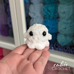 K&ouml;nnte beinhalten: Eine kleine, wei&szlig;e Pl&uuml;sch-Geisterfigur aus weichem, flauschigem Garn. Der Geist hat einen abgerundeten Kopf, zwei kleine Arme, die seitlich abstehen, und zwei gro&szlig;e, glatte, schwarze Sicherheitsaugen aus Kunststoff auf der Vorderseite.