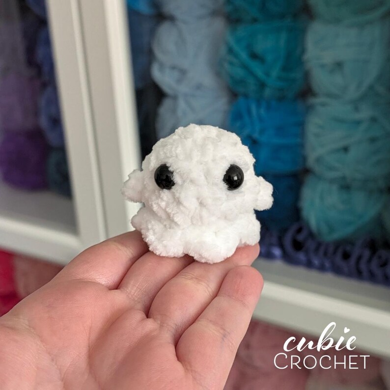 K&ouml;nnte beinhalten: Eine kleine, wei&szlig;e Pl&uuml;sch-Geisterfigur aus weichem, flauschigem Garn. Der Geist hat einen abgerundeten Kopf, zwei kleine Arme, die seitlich abstehen, und zwei gro&szlig;e, glatte, schwarze Sicherheitsaugen aus Kunststoff auf der Vorderseite.