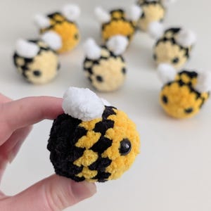 May include: Handmade crochet bees in yellow, black, and white. The bees have a round body with black and yellow stripes, white wings, and small black eyes. Several bees are visible, with one bee held in a hand.