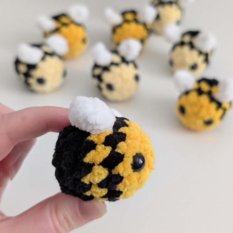 May include: Handmade crochet bees in yellow, black, and white. The bees have a round body with black and yellow stripes, white wings, and small black eyes. Several bees are visible, with one bee held in a hand.