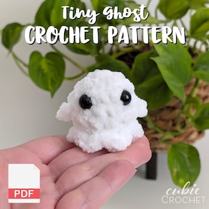 K&ouml;nnte beinhalten: Ein kleiner wei&szlig;er H&auml;kelgeist mit zwei schwarzen Kunststoffaugen. Der Text Tiny ghost CROCHET PATTERN steht oben und ein wei&szlig;es PDF-Symbol befindet sich in der unteren linken Ecke. Das Objekt besteht aus weichem, flauschigem wei&szlig;em Garn.