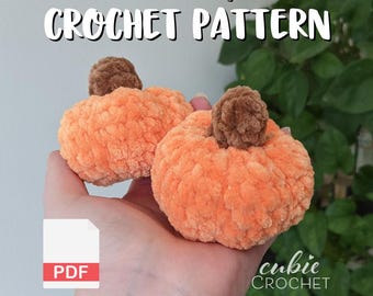 May include: Two orange crochet pumpkins with brown stems are held in a hand. The pumpkins have a textured, plush appearance. Text at the top reads "Mini Pumpkin Crochet Pattern". A PDF icon is in the lower left corner, and the "cubic CROCHET" logo is in the lower right.