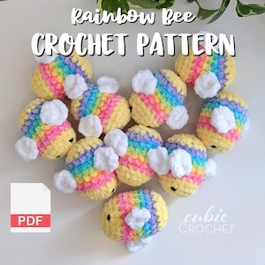 Puede incluir: Una colección de juguetes de abejas de ganchillo en colores arcoíris, con alas blancas. El texto "Rainbow Bee CROCHET PATTERN" se muestra en la parte superior. Un icono PDF está en la esquina inferior izquierda y el texto "cubic CROCHET" en la parte inferior derecha.