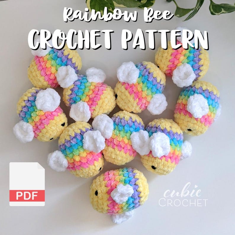 Puede incluir: Una colecci&oacute;n de juguetes de abejas de ganchillo en colores arco&iacute;ris, con alas blancas. El texto "Rainbow Bee CROCHET PATTERN" se muestra en la parte superior. Un icono PDF est&aacute; en la esquina inferior izquierda y el texto "cubic CROCHET" en la parte inferior derecha.